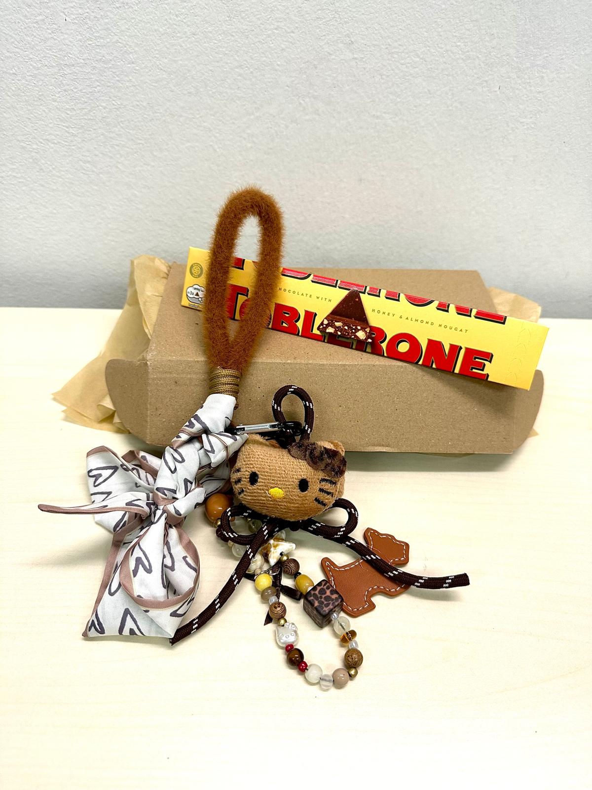 Classic Toblerone chocolate bar with honey and almond nougat next to a cute cat-themed keychain with beads and ribbon.